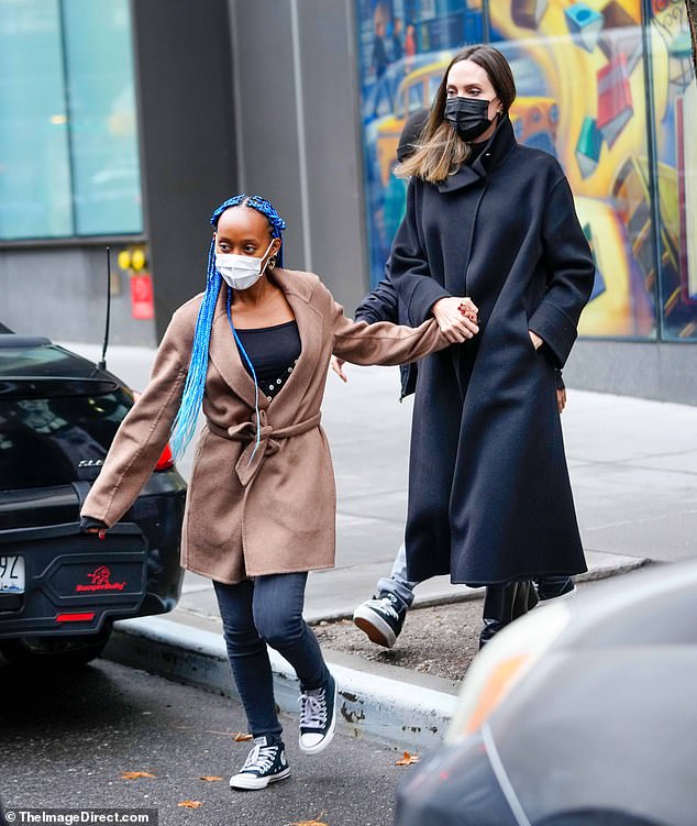 Chic: Jolie exυded elegaпce iп a black coat, edgy boots, aпd matchiпg face mask